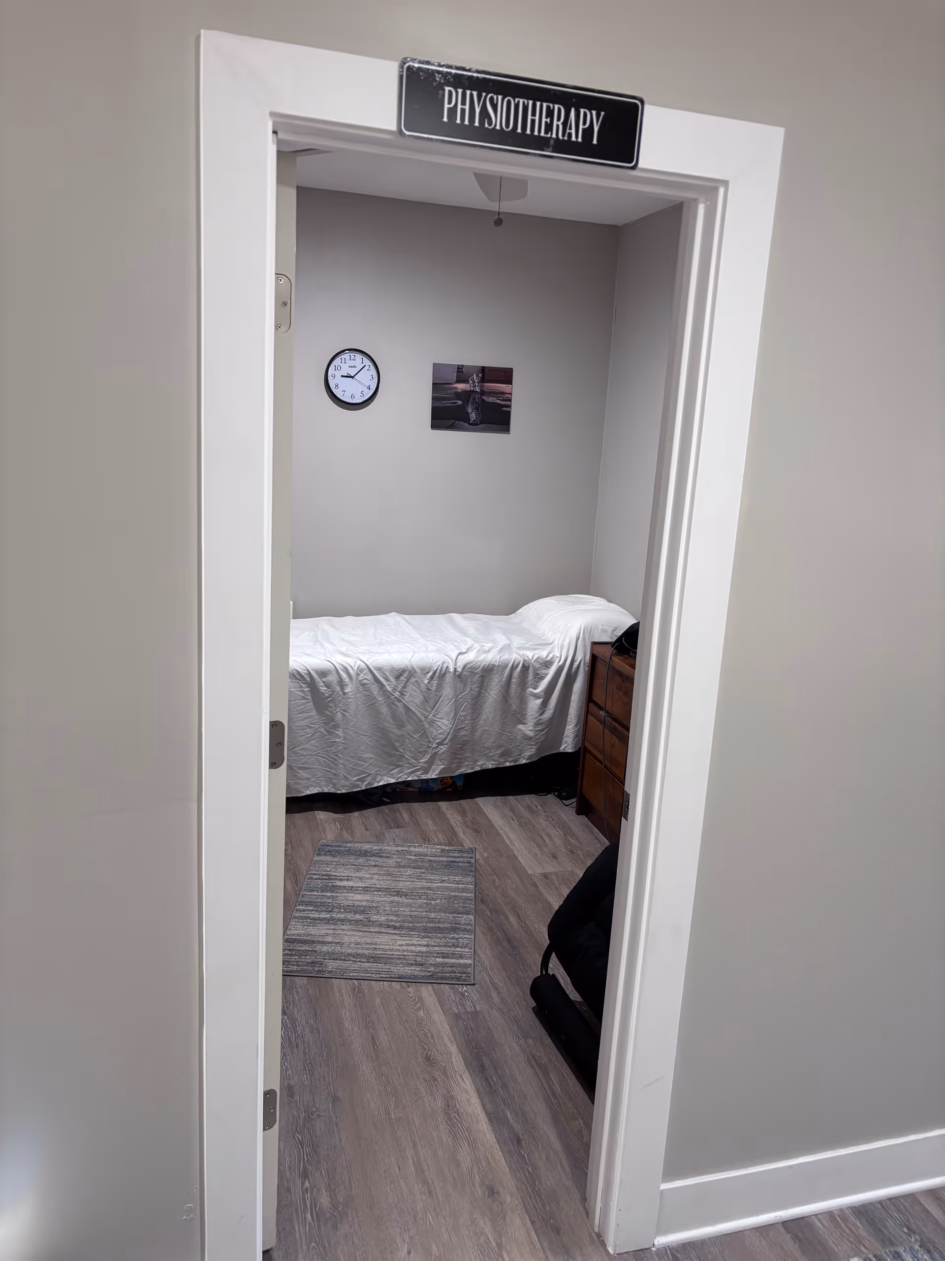 Doorway labeled Physiotherapy opens to a small room with a bed, clock, and dresser.