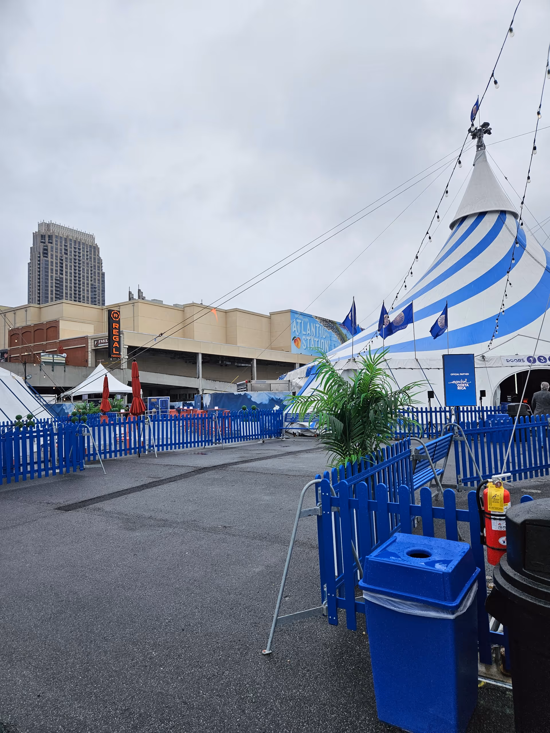 Outdoor festival setup with blue fences, tents, and string lights in a paved area.