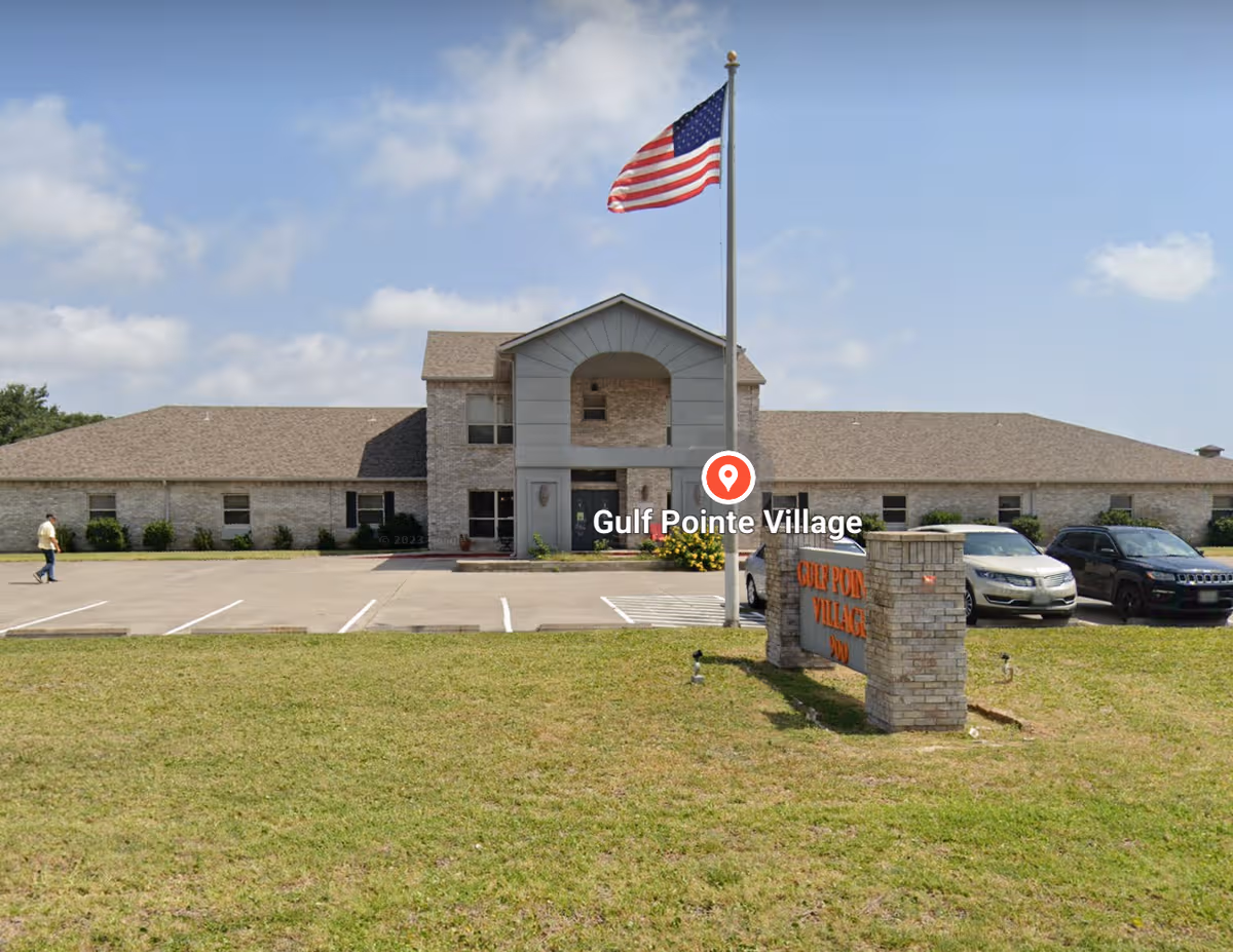 Front view of Gulf Pointe Village with flagpole, American flag, and parking lot.