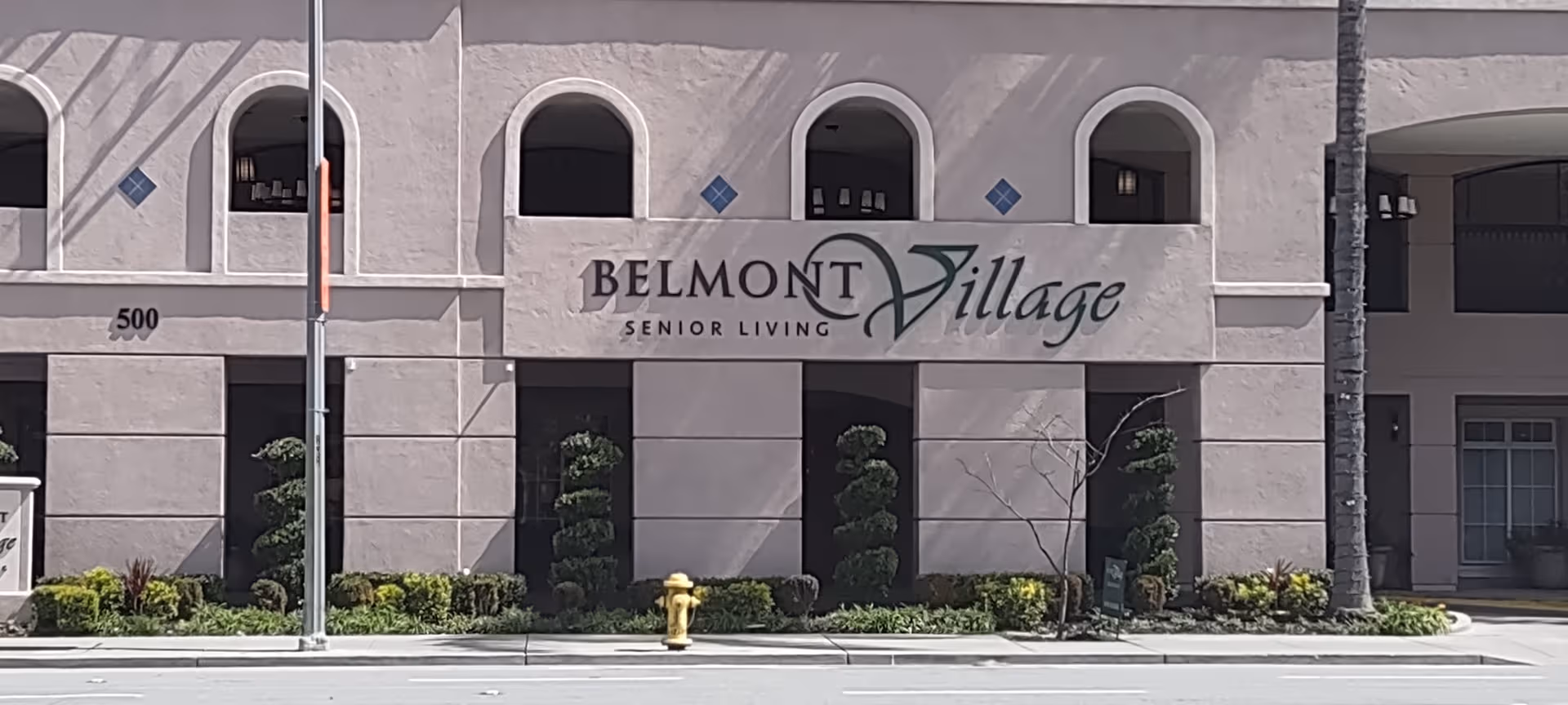 Exterior view of Belmont Village Senior Living building with arched windows and landscaping.