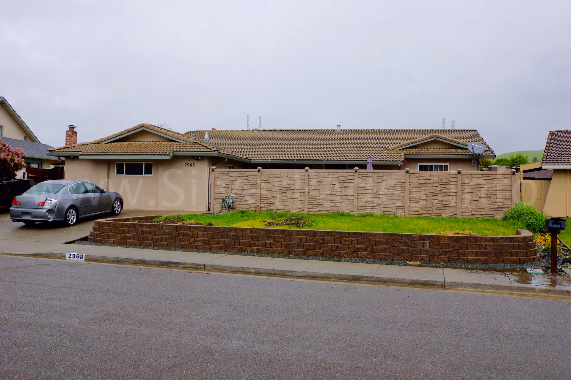 Single-story senior living facility with brick front, low retaining wall, green lawn, and parked car.