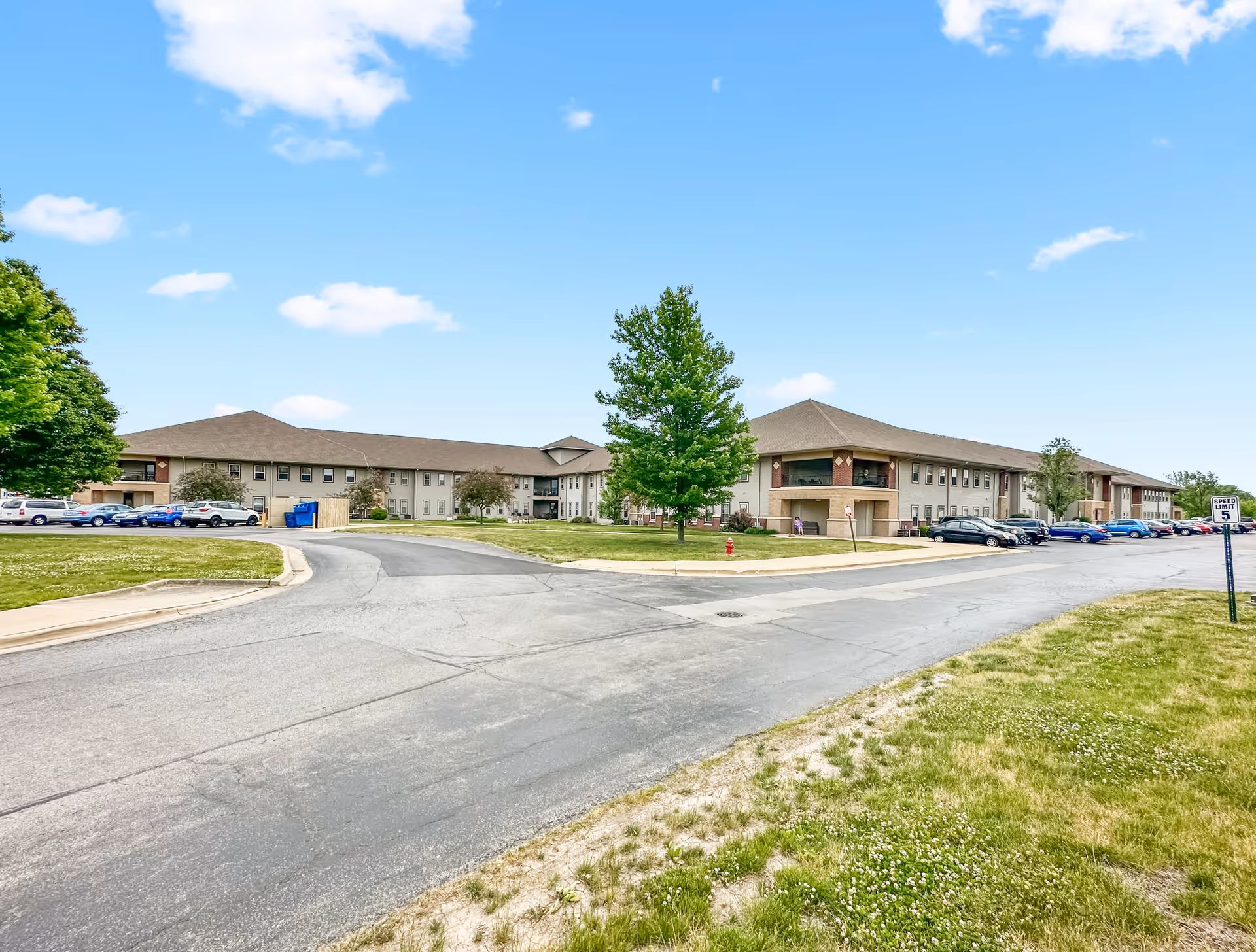 Exterior of a low-rise senior apartments building with a curved driveway and parked cars.