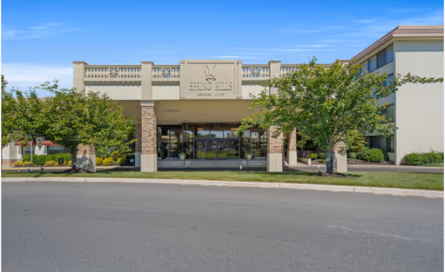 Front entrance of a multi-story senior living building with a covered porte-cochere, glass doors, and landscaping.