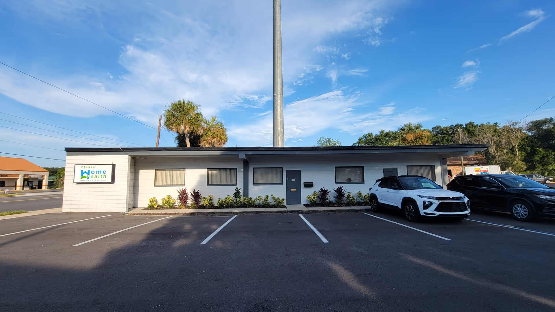 Single-story Classic Home Health facility with parking, palm trees, and blue sky.