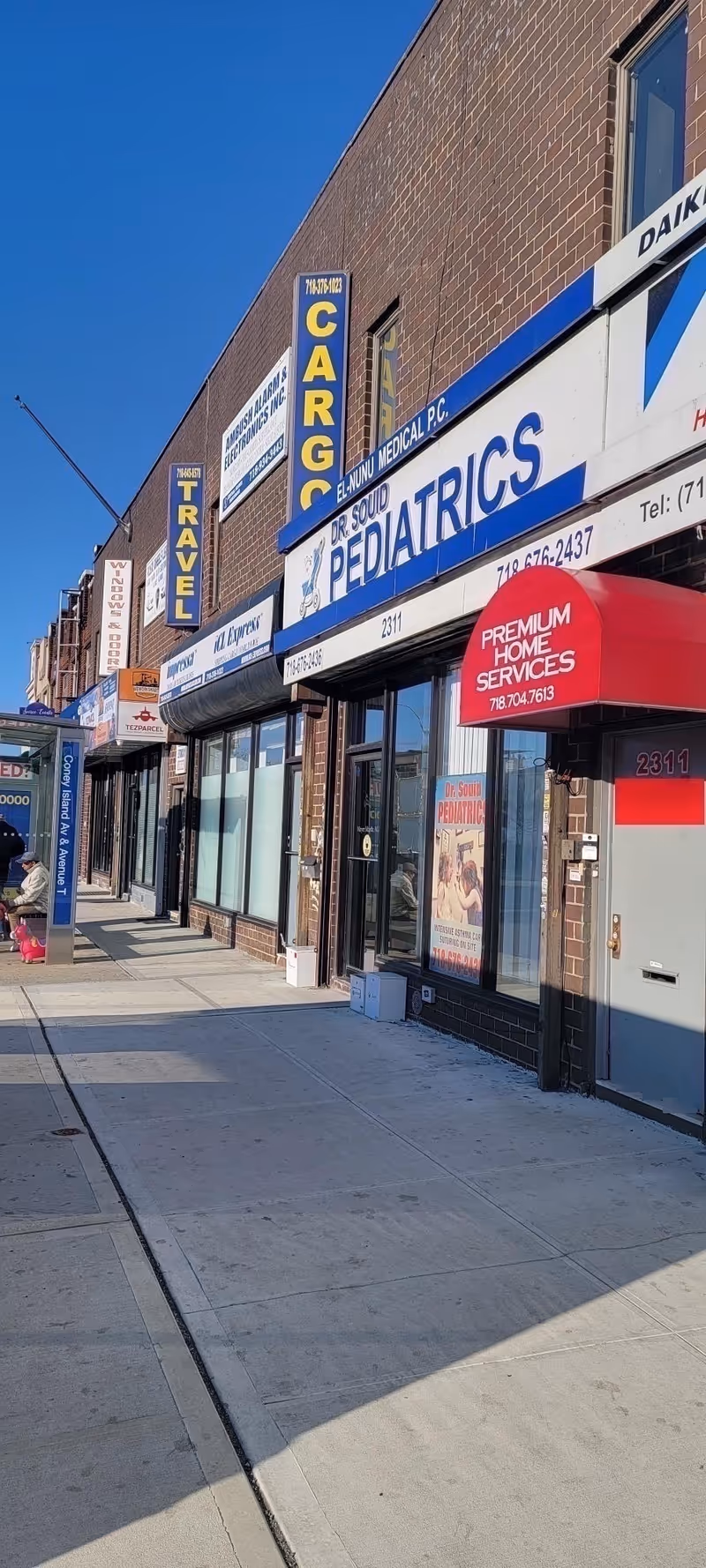 Brick storefronts along the sidewalk with pediatrics sign and Premium Home Services awning.
