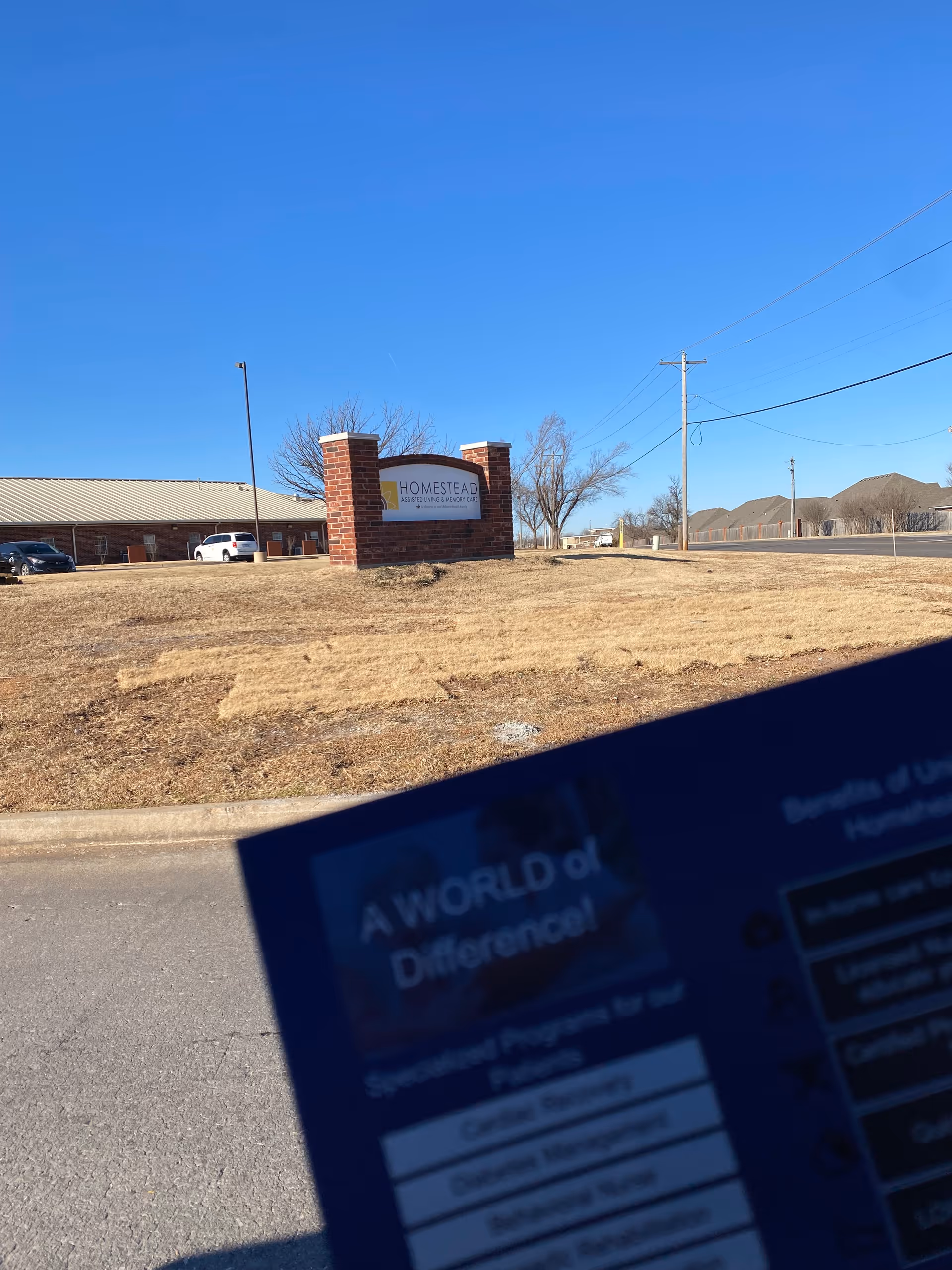 Front exterior of a facility with a brick sign and building in the background.