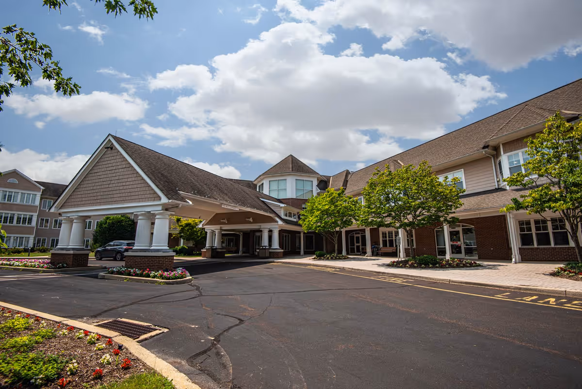 Front entrance and porte-cochere of the Horsham Center for Jewish Life with a paved driveway, landscaping, and trees under a partly cloudy sky.