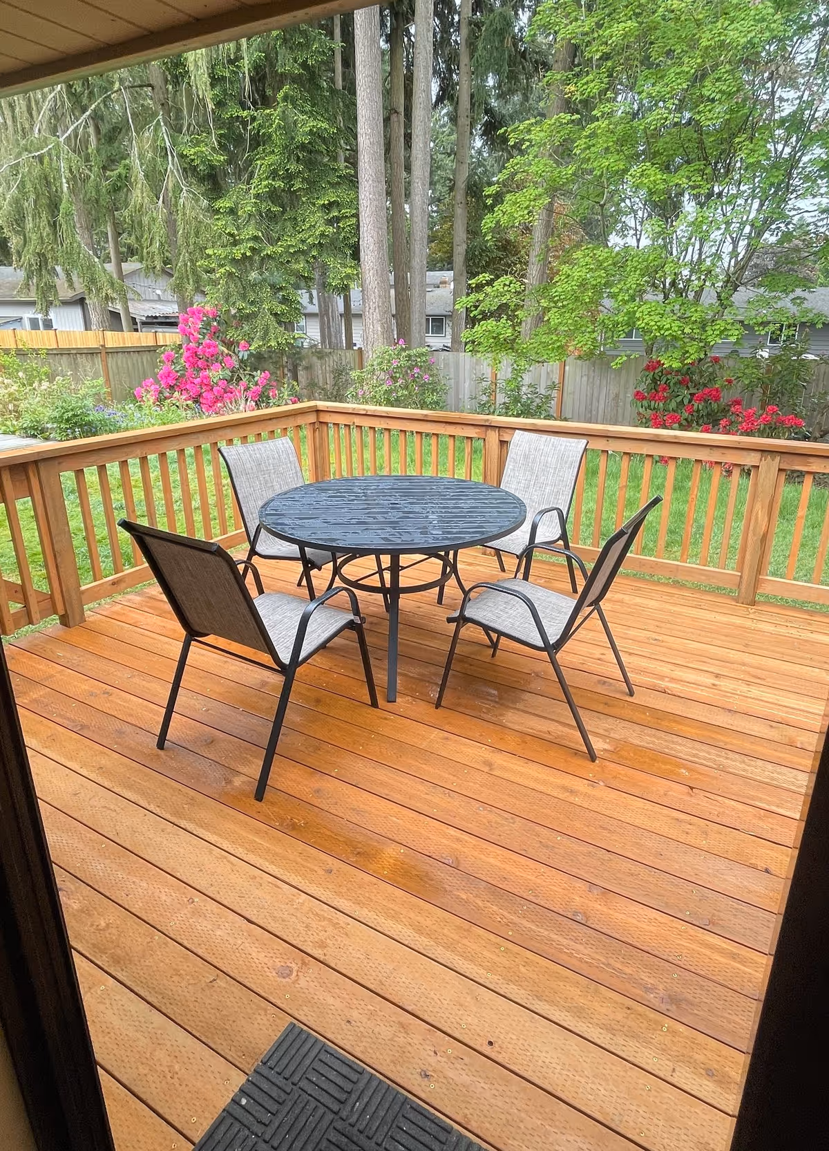 An outdoor wooden deck with a round table and chairs amid greenery.