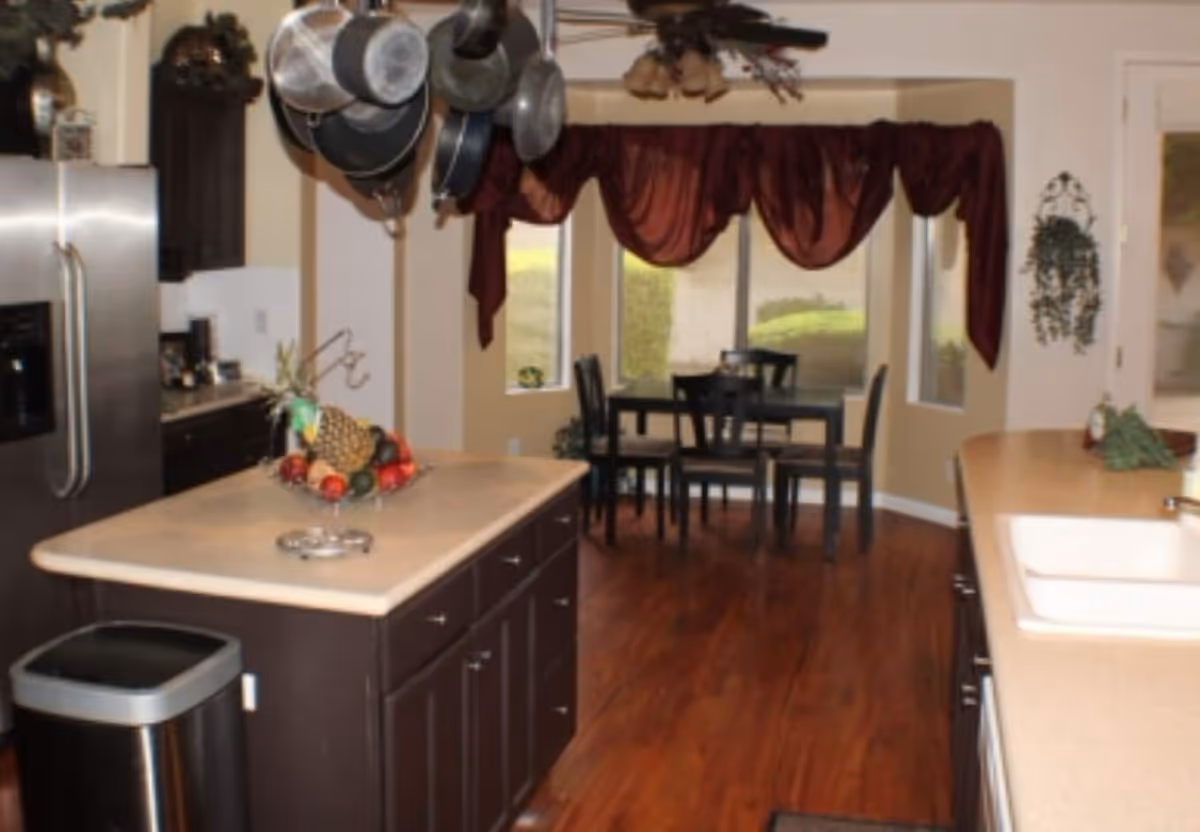 Kitchen with island, fruit bowl, stainless fridge, and a dining area visible in the background.