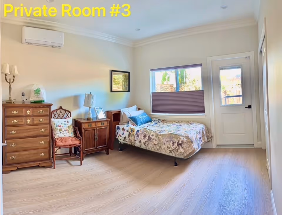 A furnished private bedroom with a bed, dresser, chair, nightstand, window, and door.