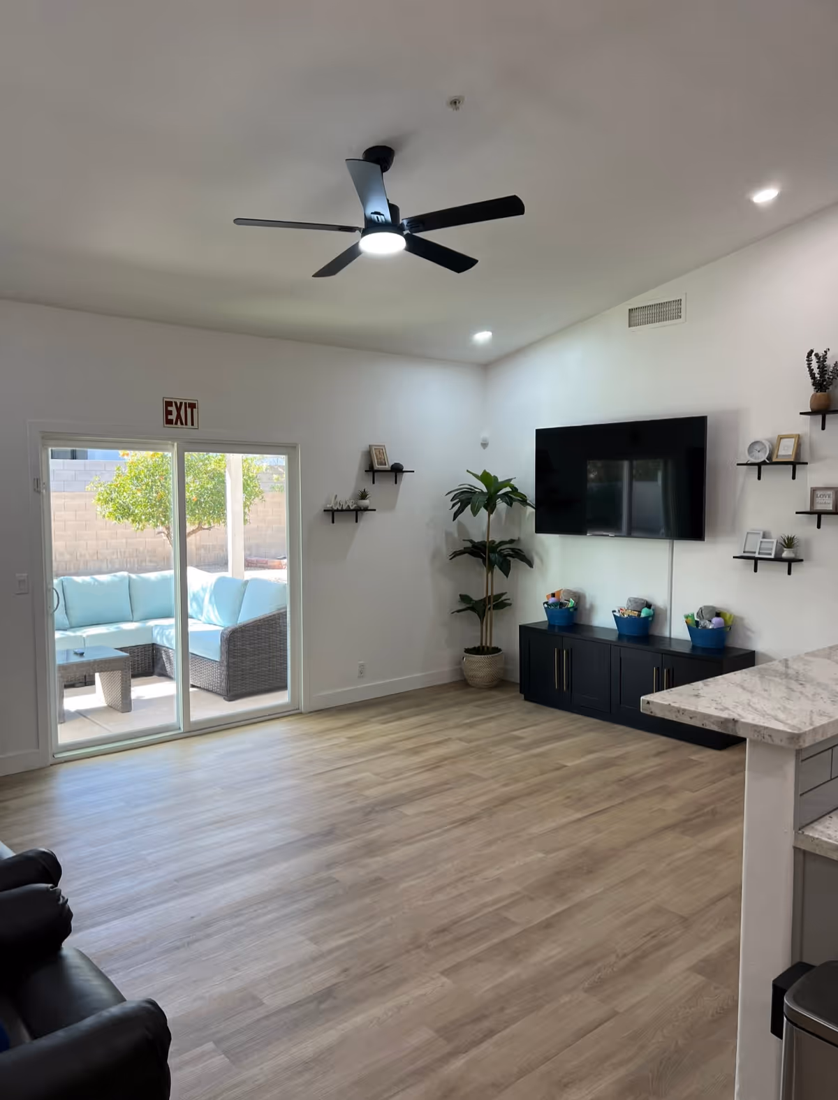 Spacious living room with ceiling fan, TV, shelves, and sliding glass door to outdoor patio.