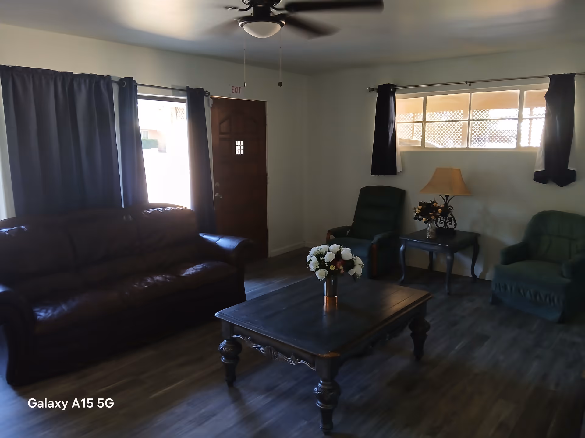 Cozy living room with leather sofa, green chairs, a wooden coffee table, and flowers.