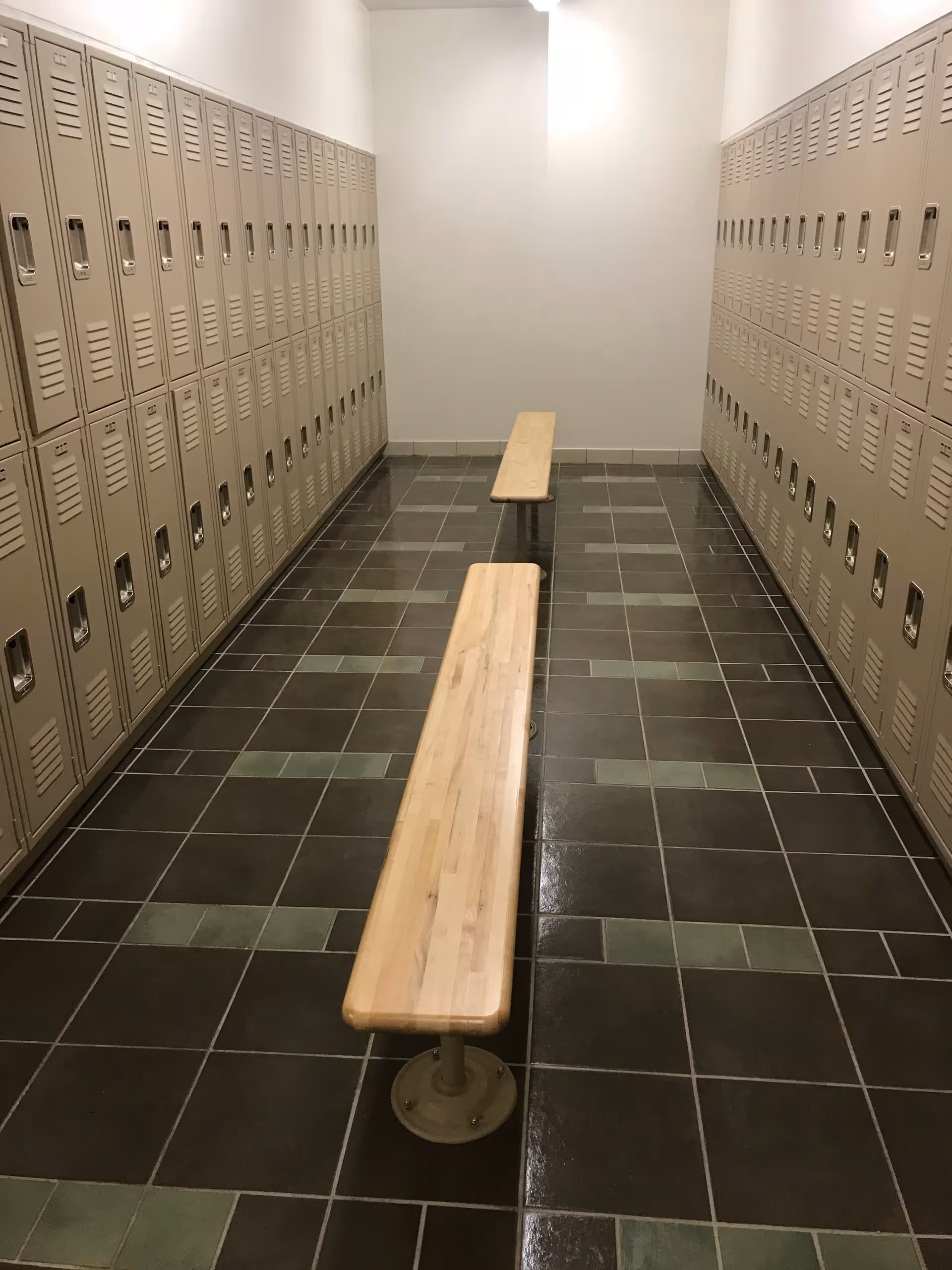 Long hallway with beige lockers lining both walls and two wooden benches in center.