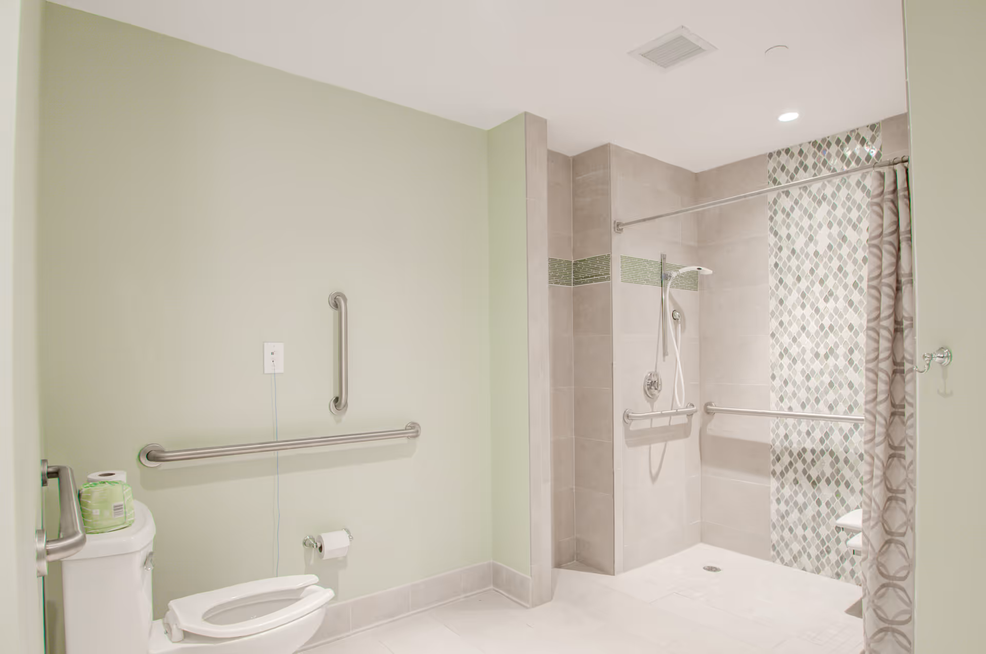 Accessible bathroom with green walls, toilet, and walk-in shower with grab bars.