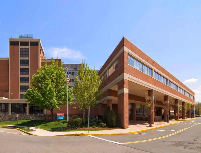 Exterior view of Middlesex Hospital brick building with a covered entrance and surrounding trees.
