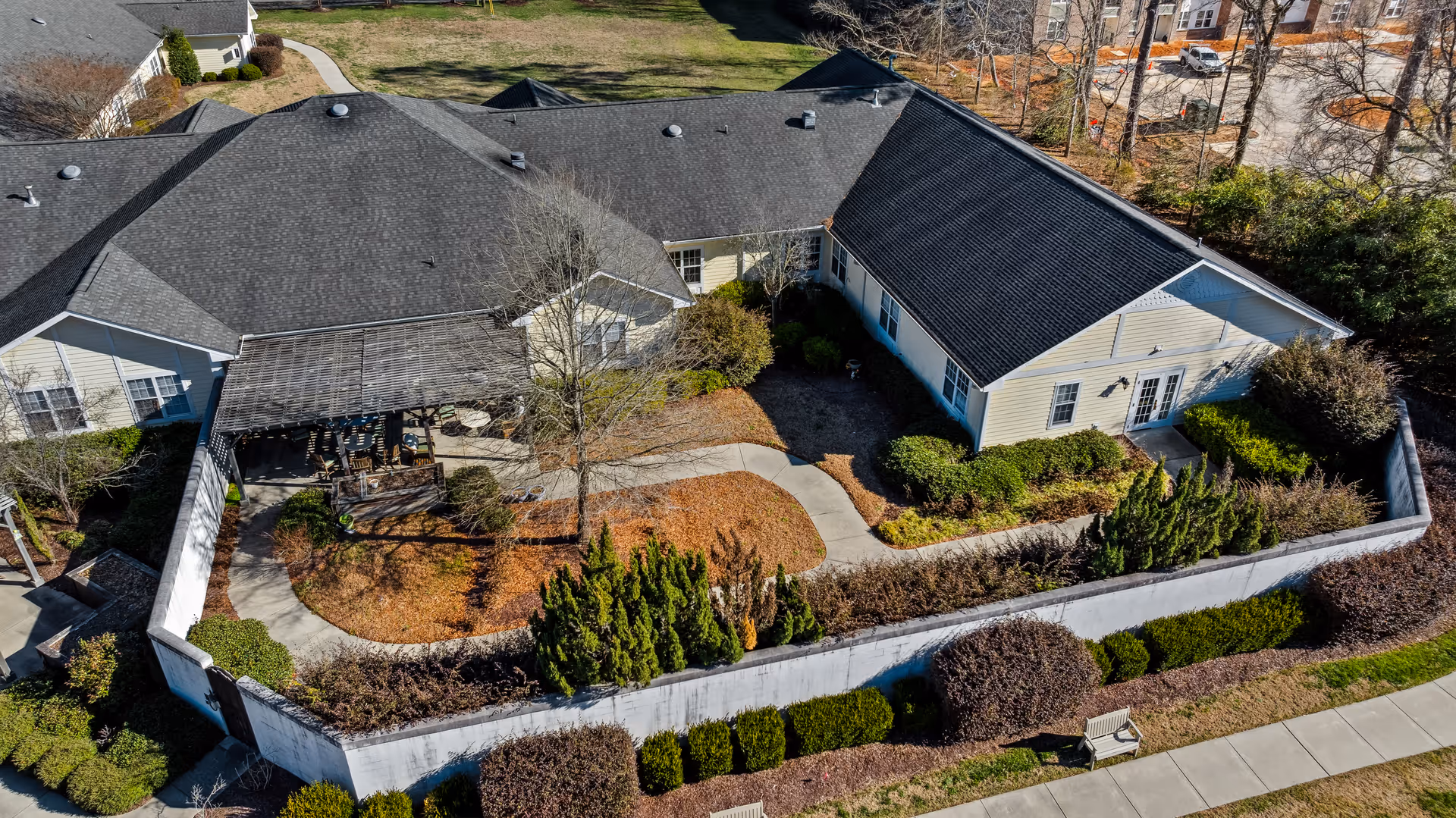 Aerial view of a gated courtyard at a single-story senior living facility with a pergola-covered patio, walkways, and landscaped shrubs.