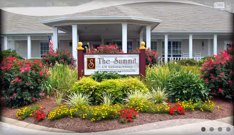 Front entrance of The Summit At Home senior living facility with landscaped flower beds and sign.