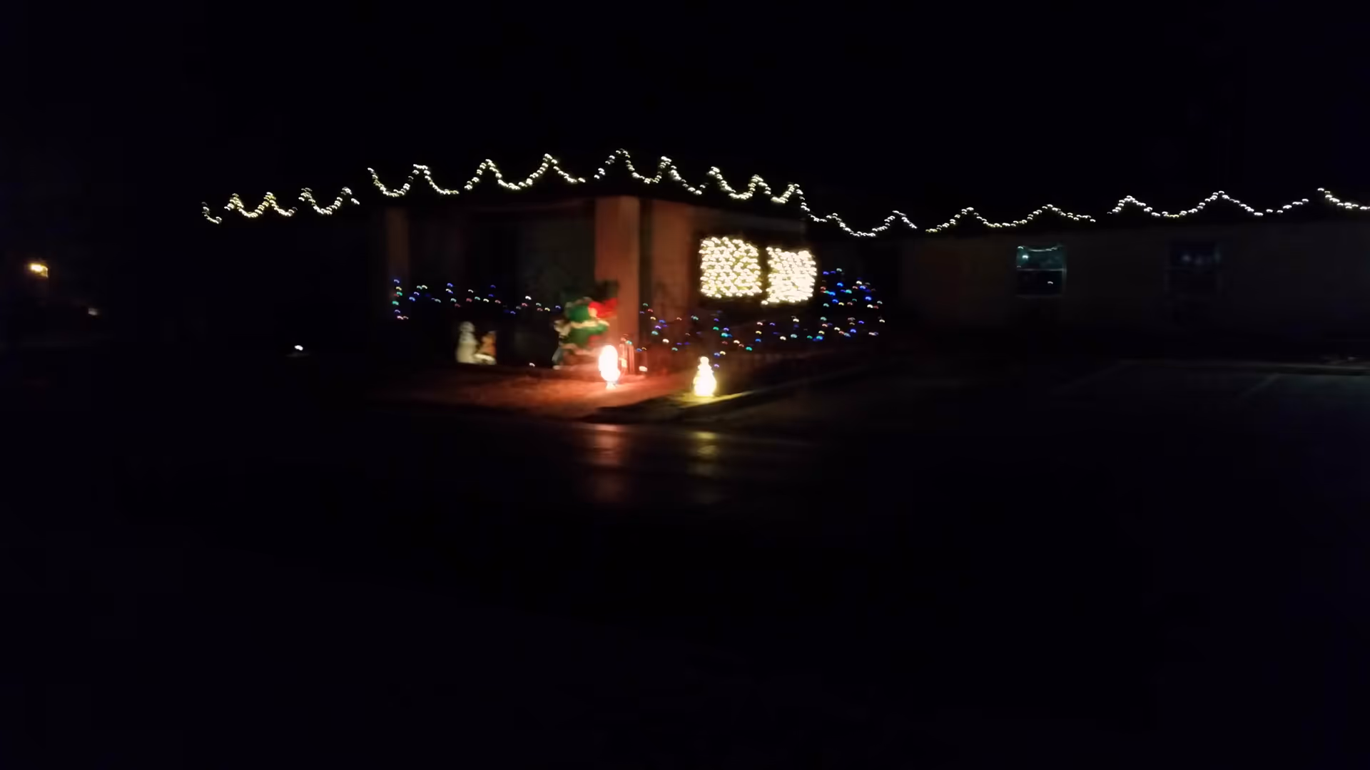 Dark exterior of a building decorated with Christmas lights and illuminated figures.
