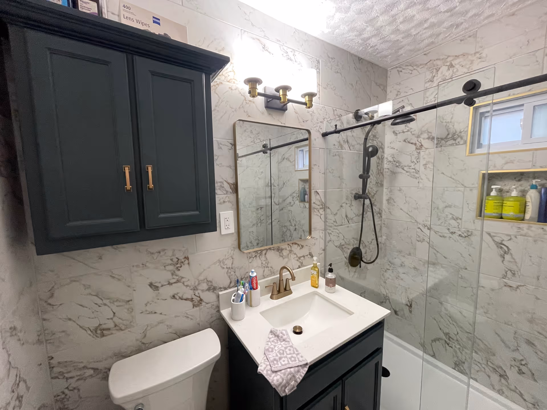 A marble-tiled bathroom with a dark vanity, mirror, and glass shower enclosure.