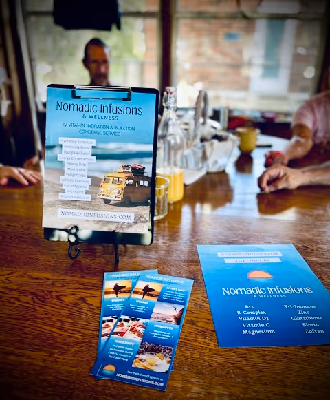 Promotional display and brochures for Nomadic Infusions and Wellness on a wooden table.