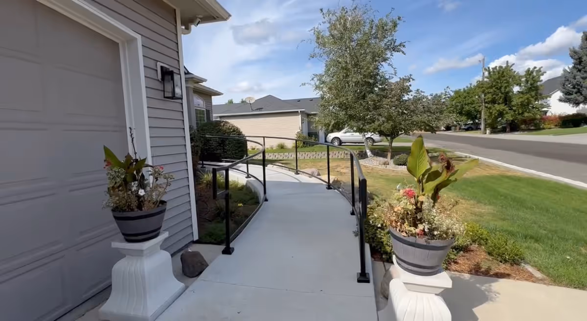 Curved concrete ramp with black railings leads to the front entrance of a gray residence.