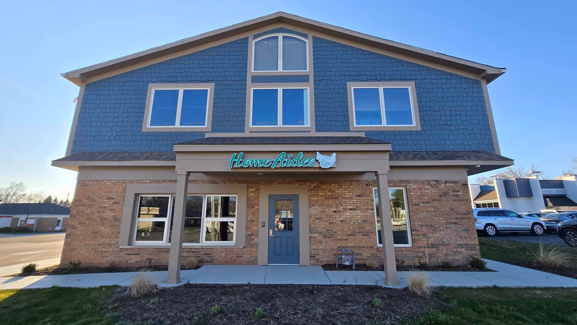 Two-story brick building with blue siding and a covered entrance marked HomeAides.