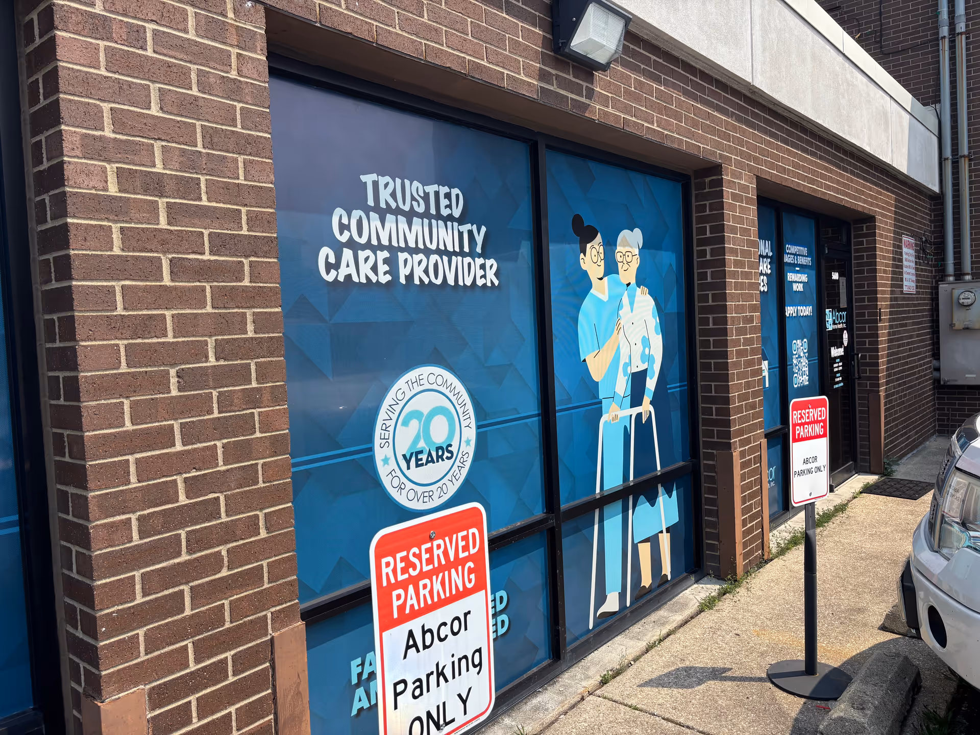Outside storefront of Abcor Home Health with illustrated caregivers on windows and reserved parking signs.