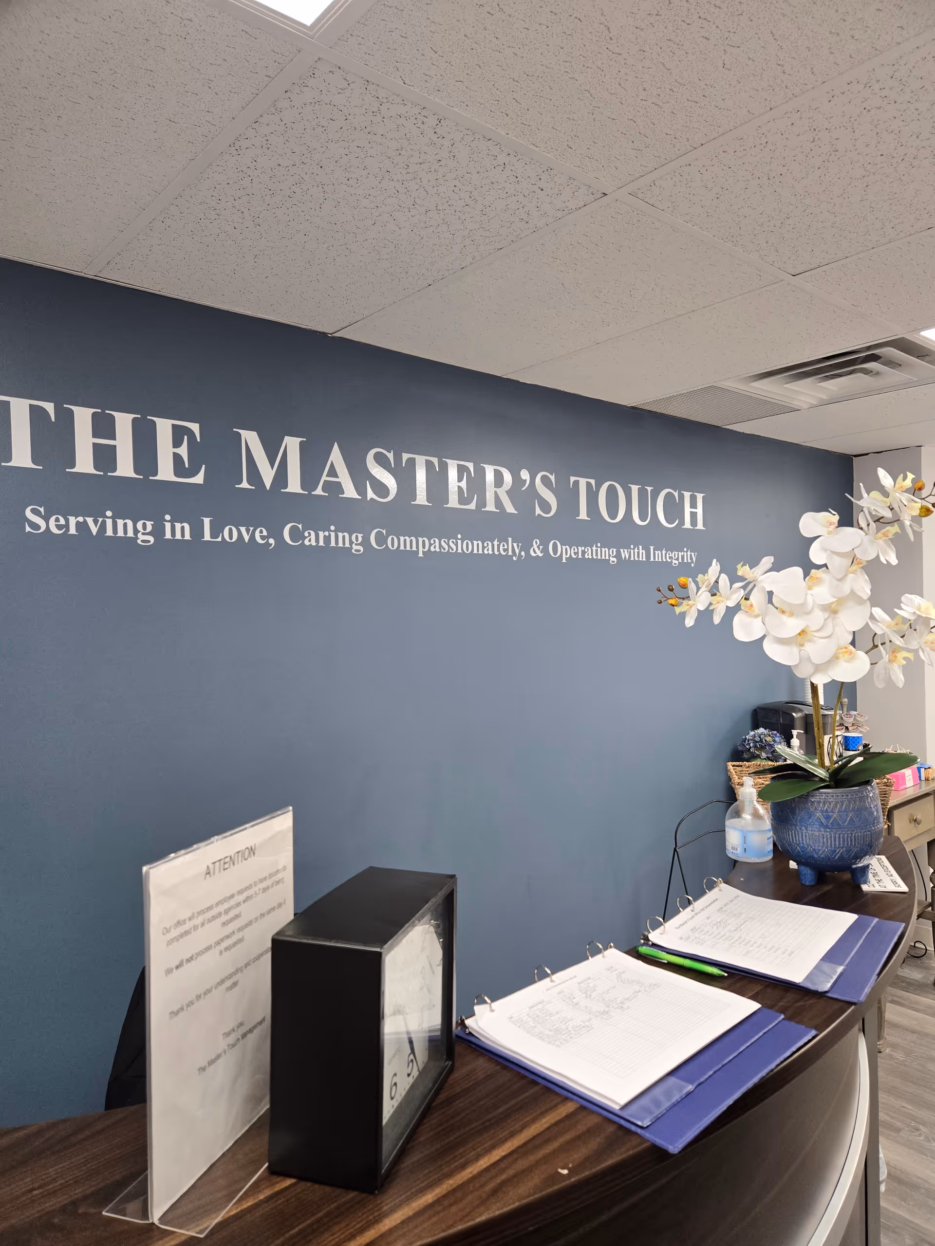 Reception desk in a blue lobby with The Master's Touch sign and orchid plant.