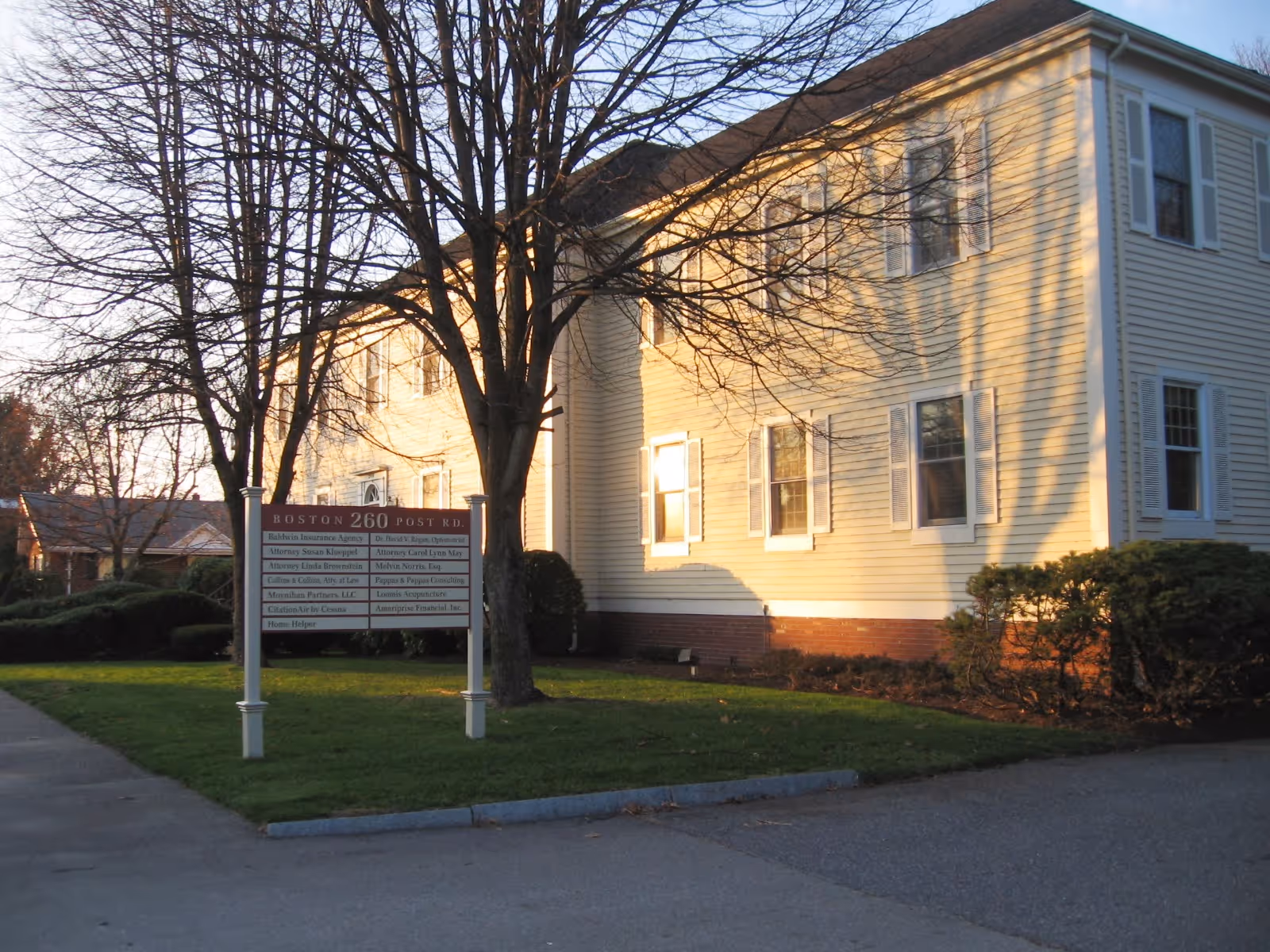 Two-story beige building with white trim and a sign in the front lawn.
