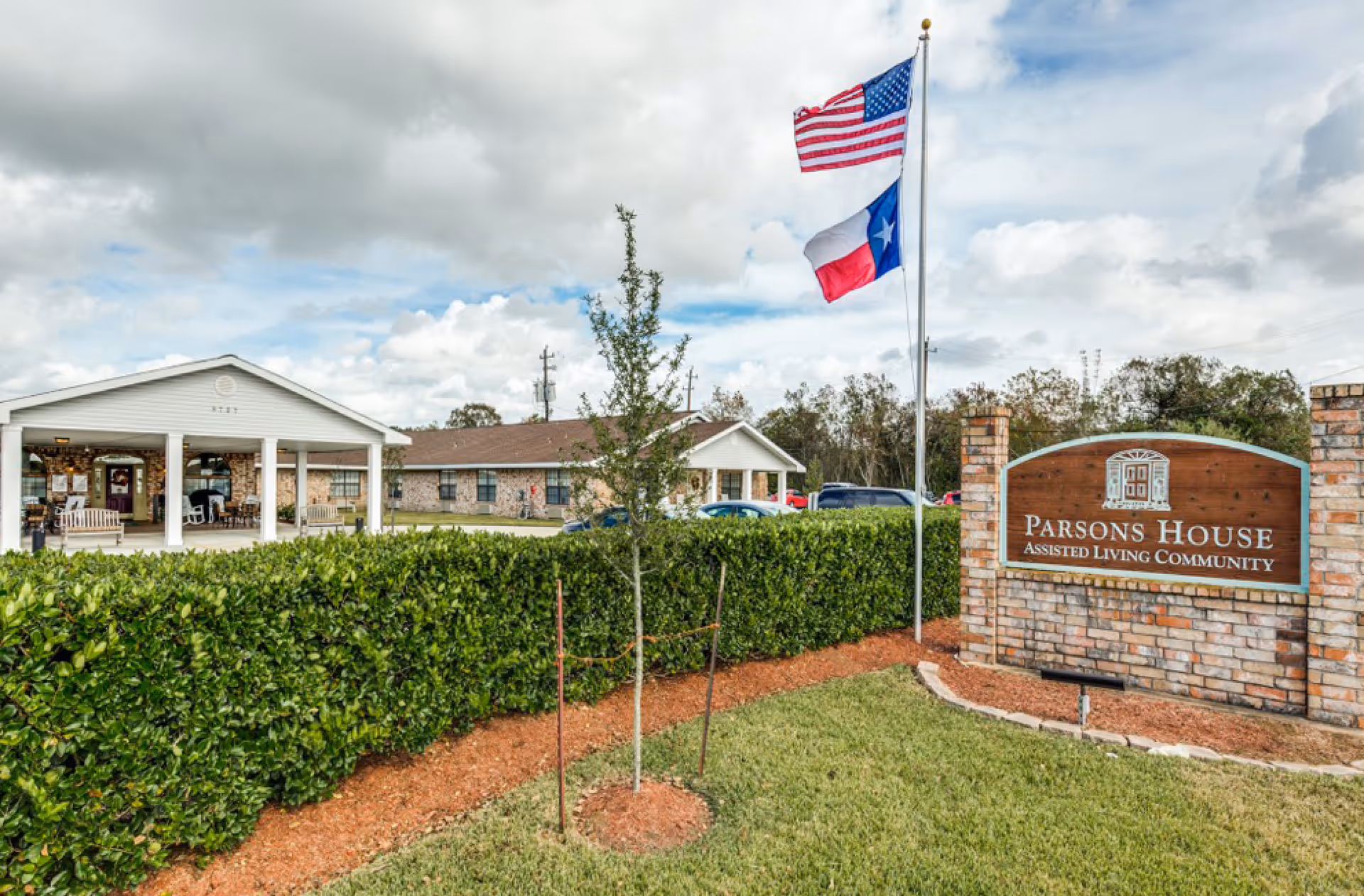 Entrance and sign for Parsons House Assisted Living Community with American and Texas flags in front of a single-story building.