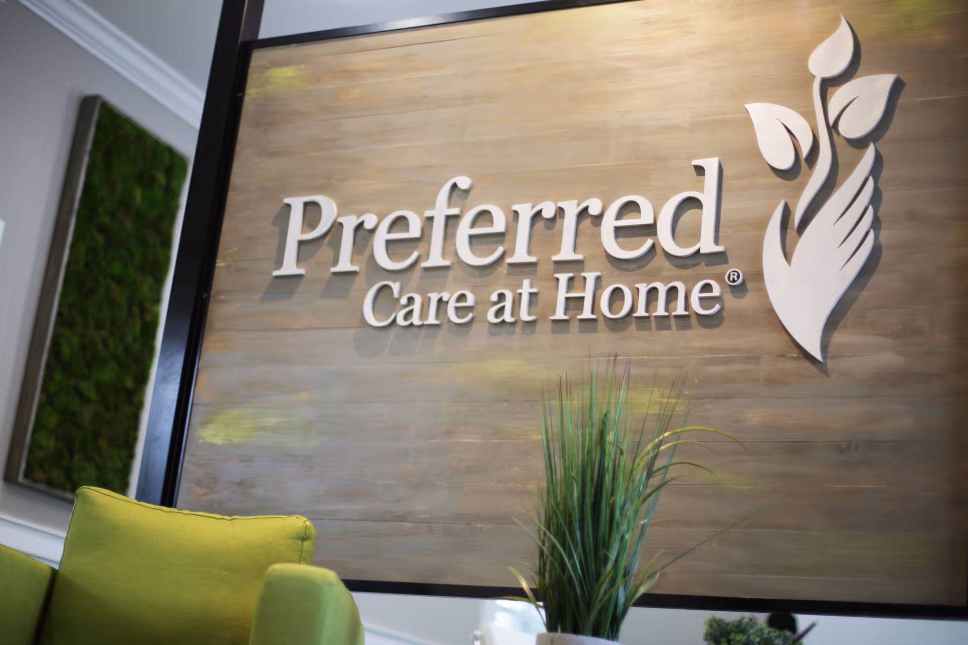 Lobby interior with a wood panel wall sign reading 'Preferred Care at Home' and green seating.