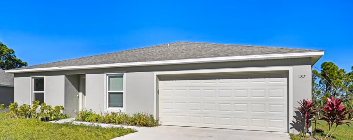 A single-story light-gray building with a double garage and a manicured lawn.