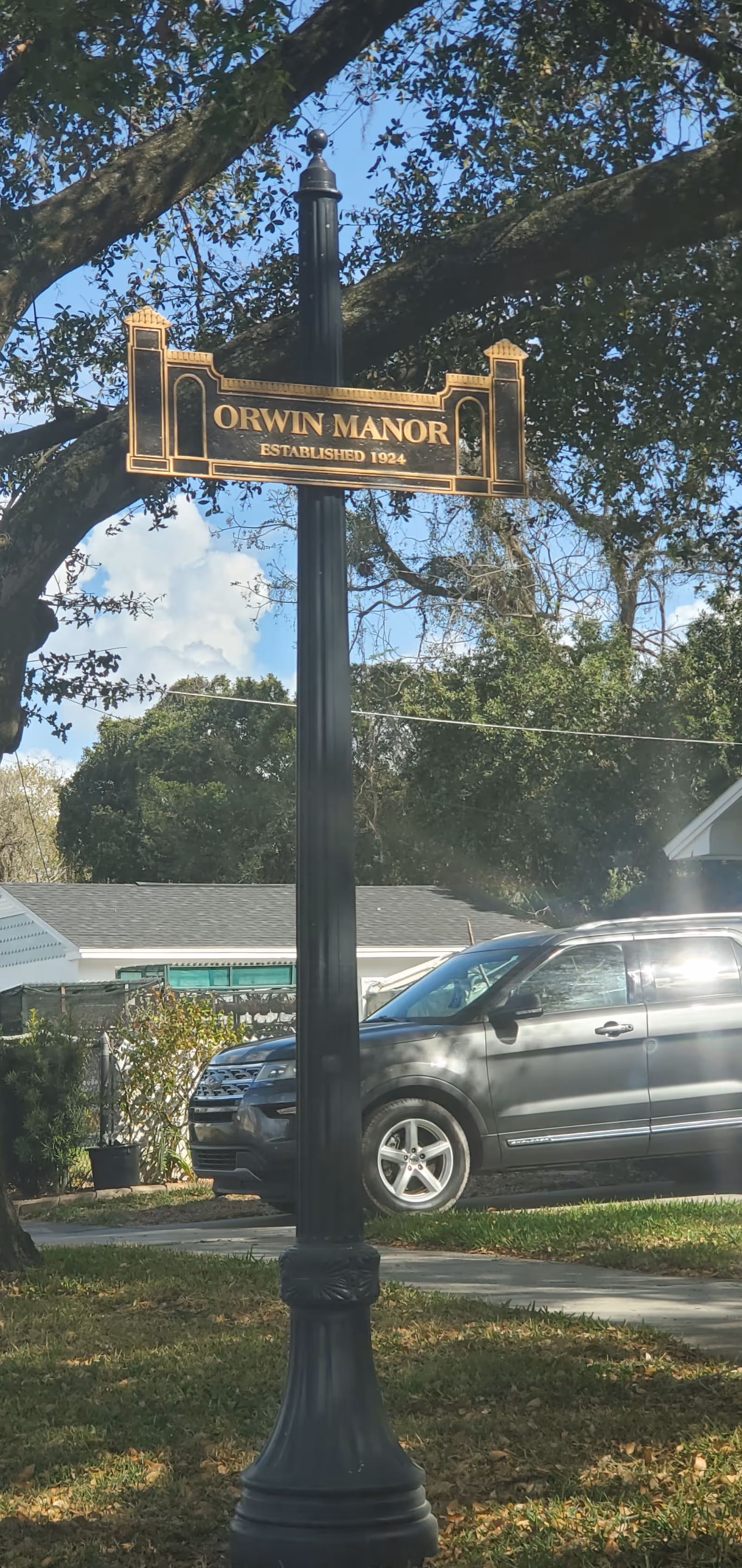 Orwin Manor street sign on a lamppost with trees and a parked SUV.