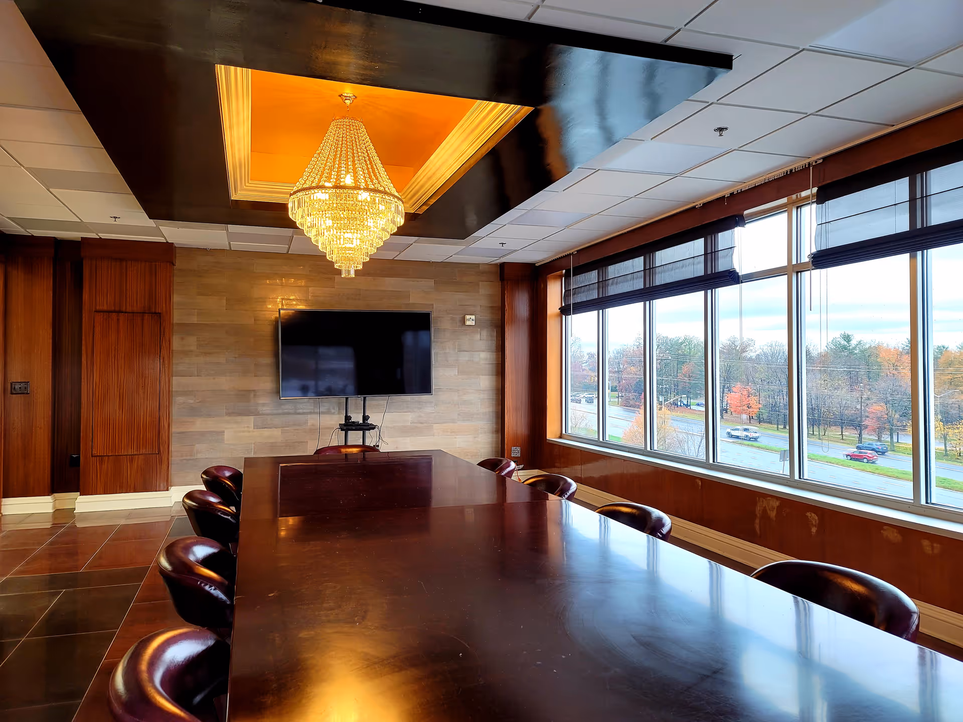 Long polished conference table with leather chairs, chandelier, and large windows in a meeting room.