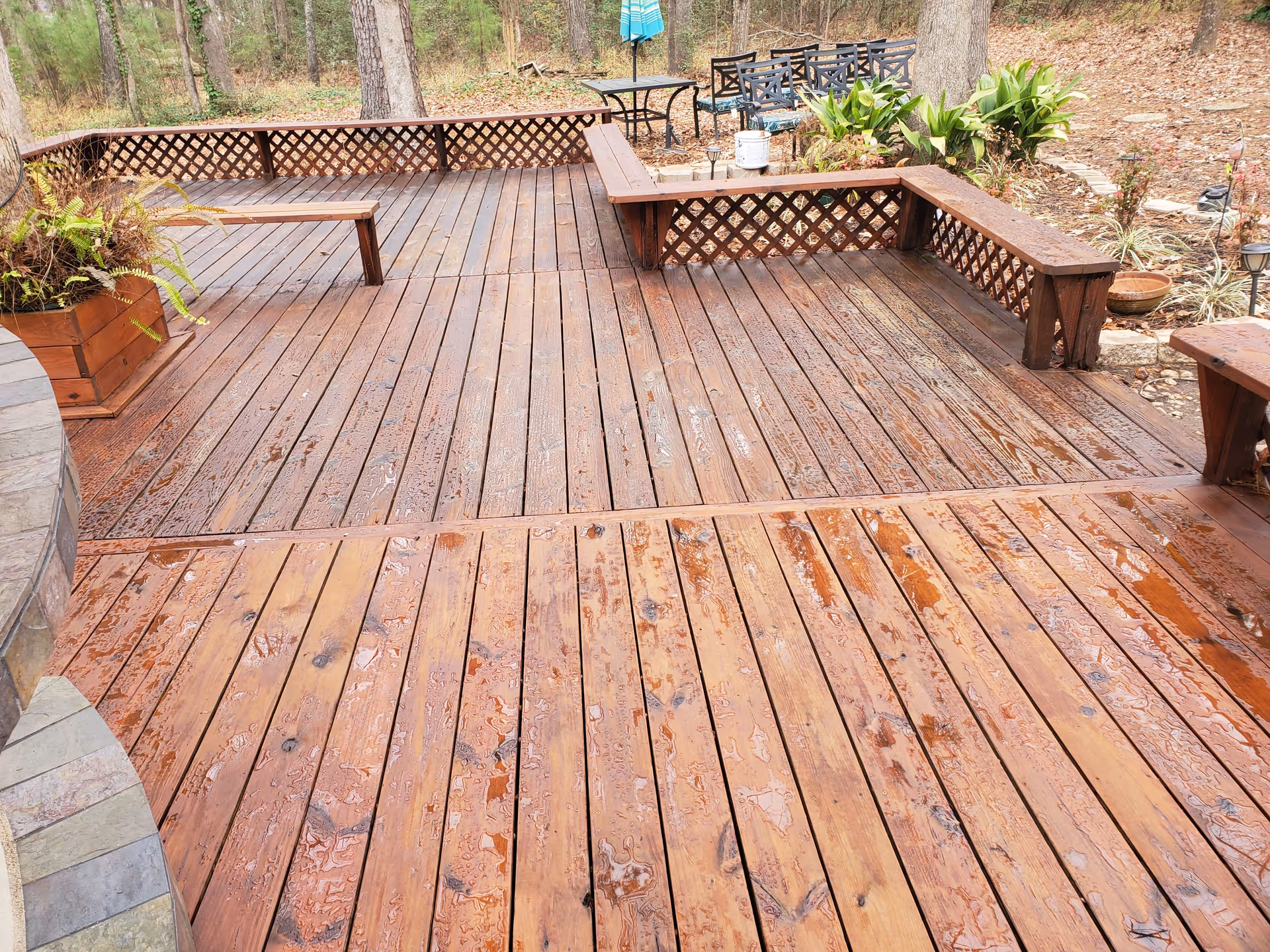 Wet wooden outdoor deck with built-in benches, planters, and surrounding trees