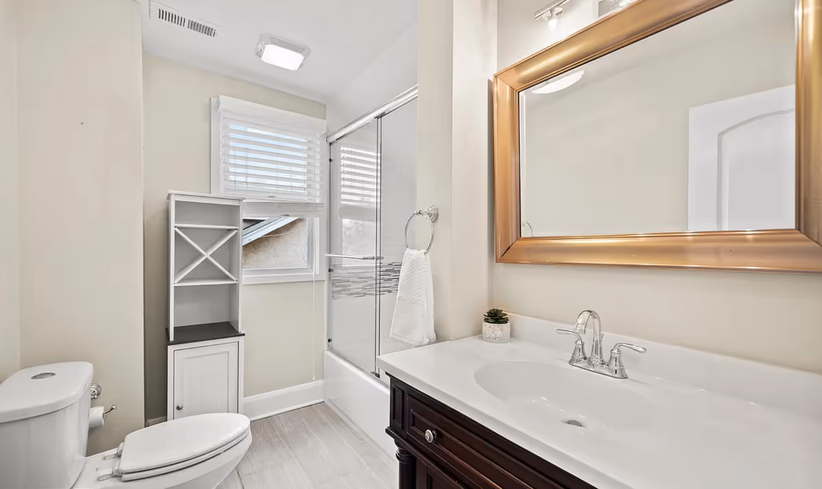 Neutral-toned bathroom with toilet, vanity, mirror, and glass-enclosed shower