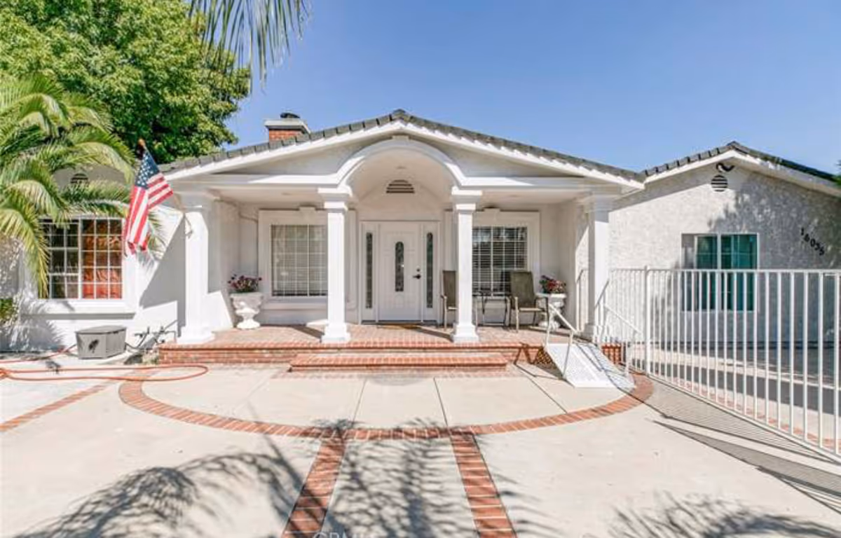 White single-story building with front porch, columns, steps, and an American flag.