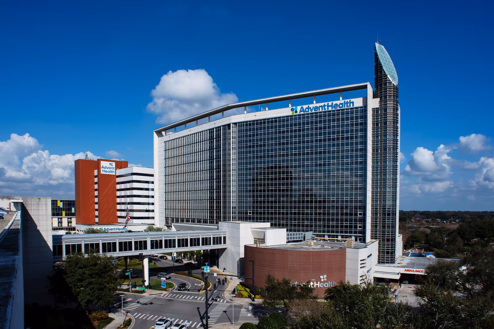 Tall glass AdventHealth hospital exterior under a bright blue sky.