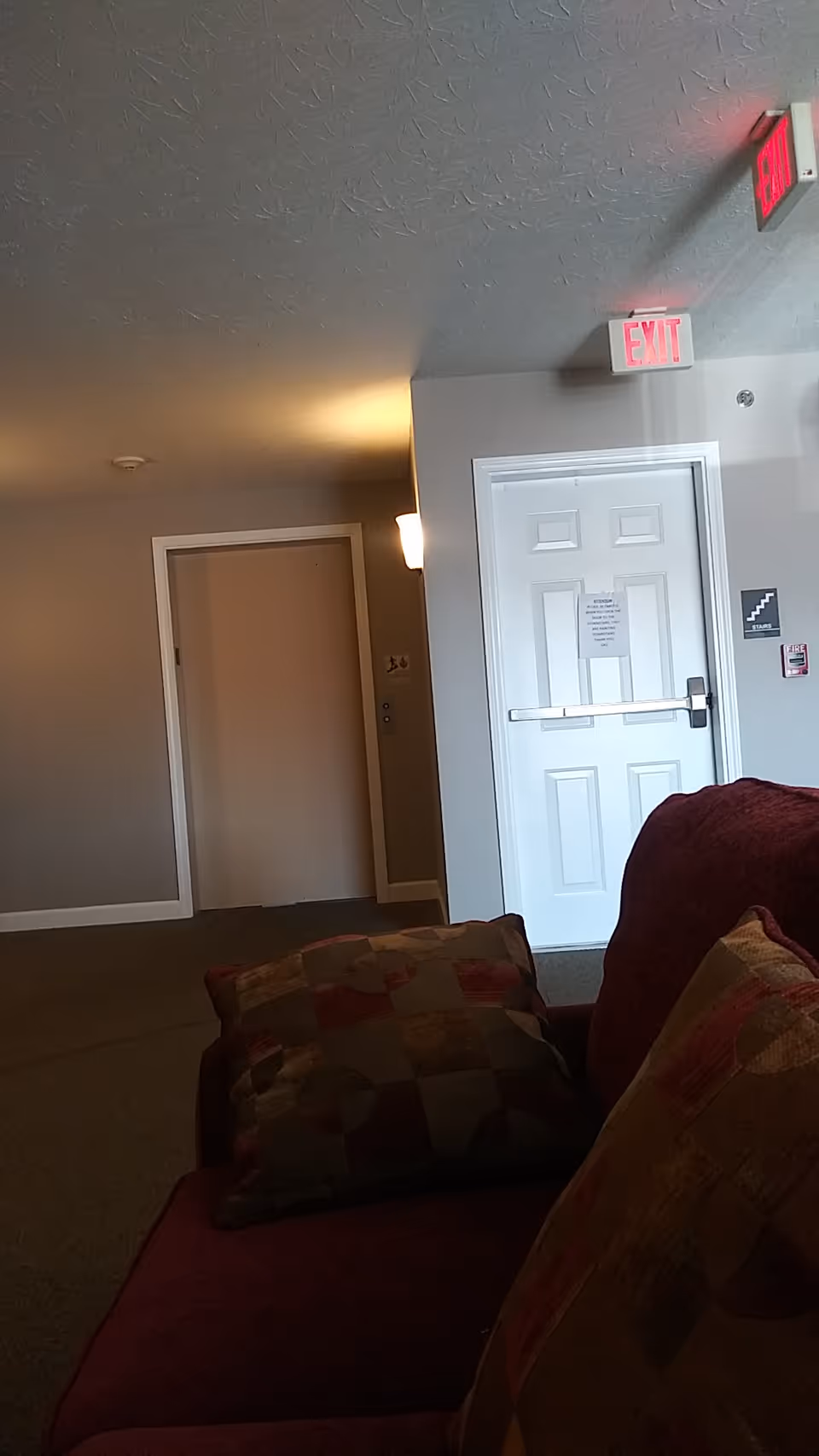 Indoor lounge area of a senior housing facility with a couch, cushions, and hallway doorway.