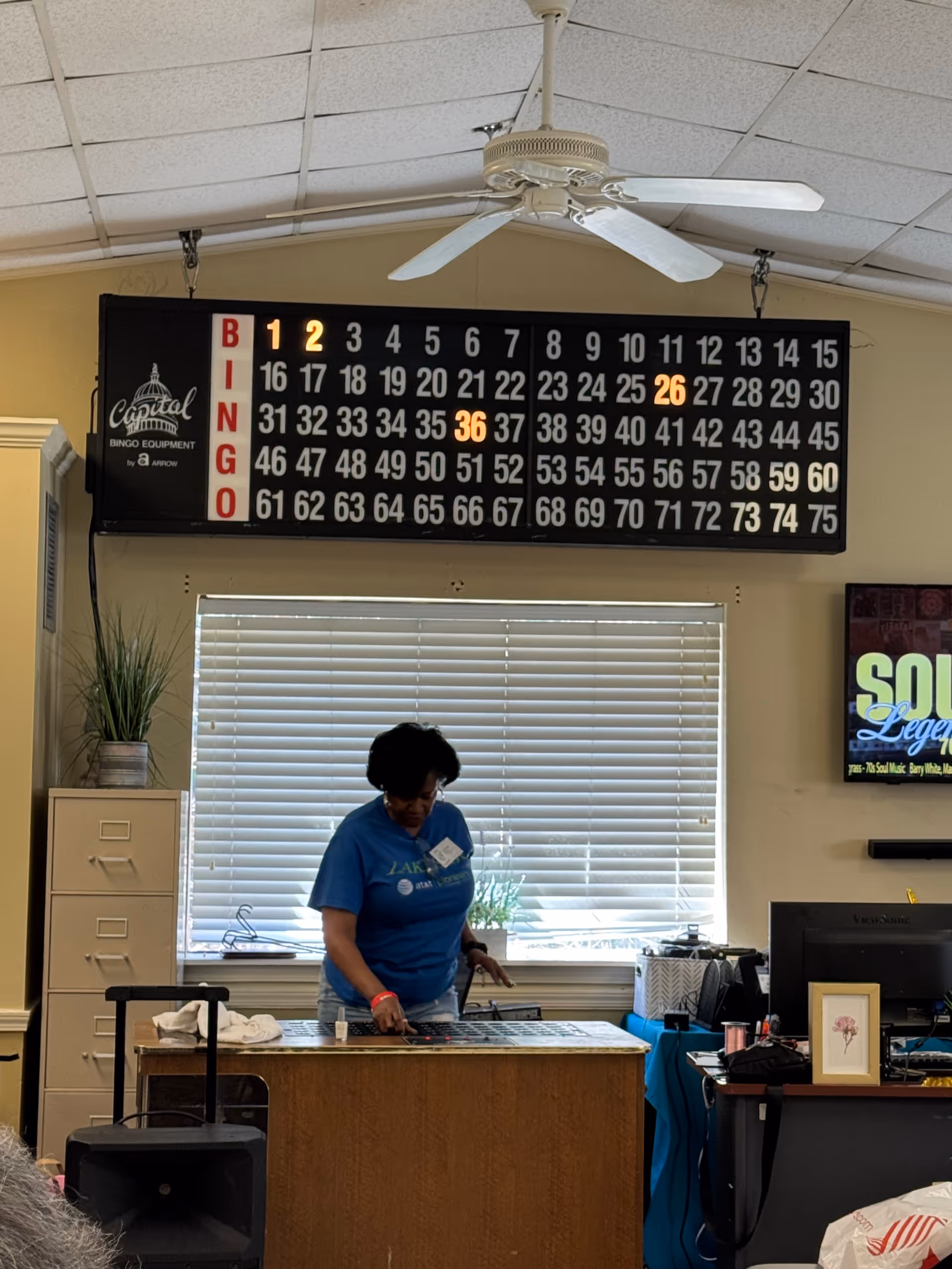 Indoor senior living lounge showing a large bingo board and a staff member organizing cards