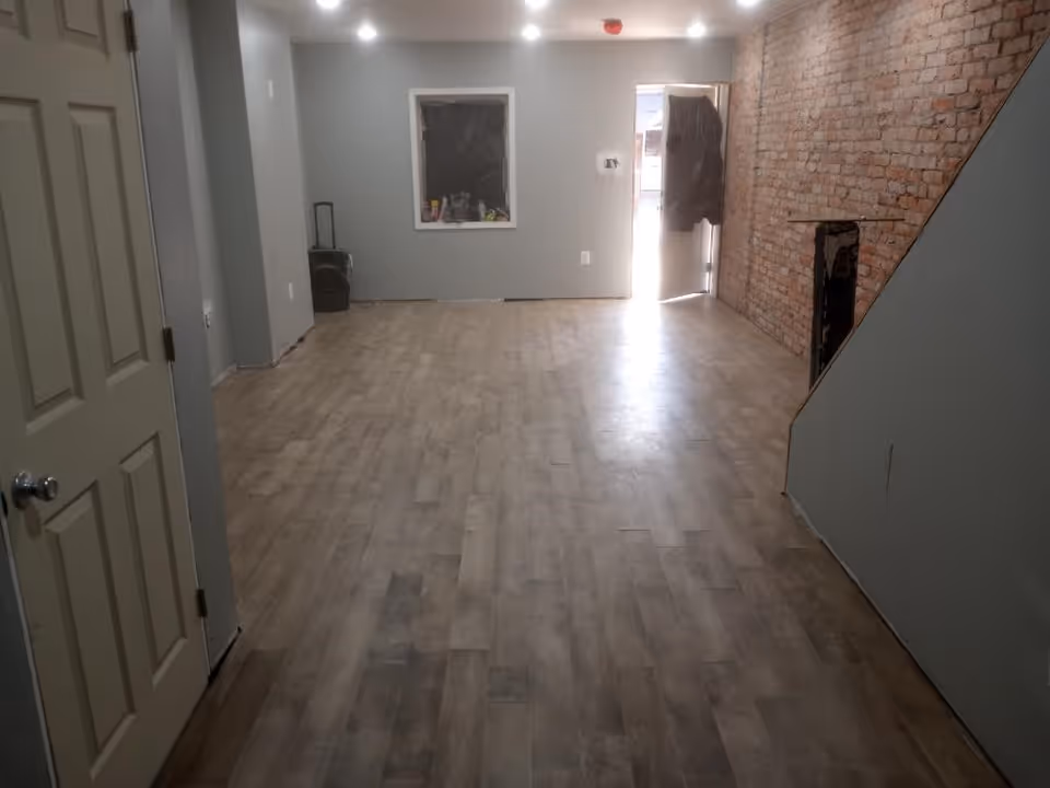 Spacious unfinished interior with gray walls, brick accent, and back door.