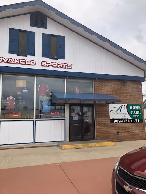 Exterior storefront with large windows, blue awning, and 'Advanced Sports' sign on brick building.