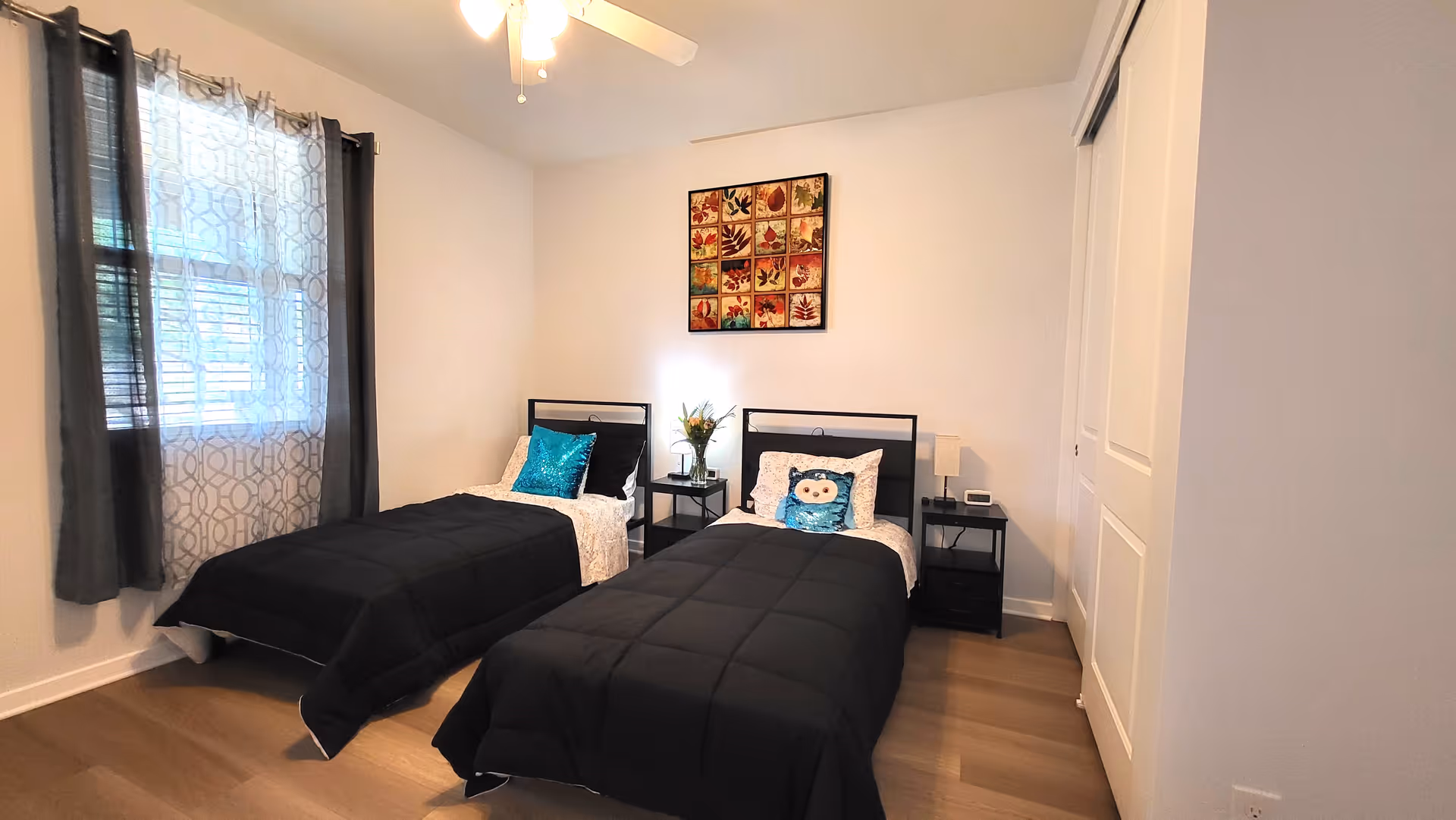 Two twin beds with black comforters and matching nightstands in a bright bedroom.