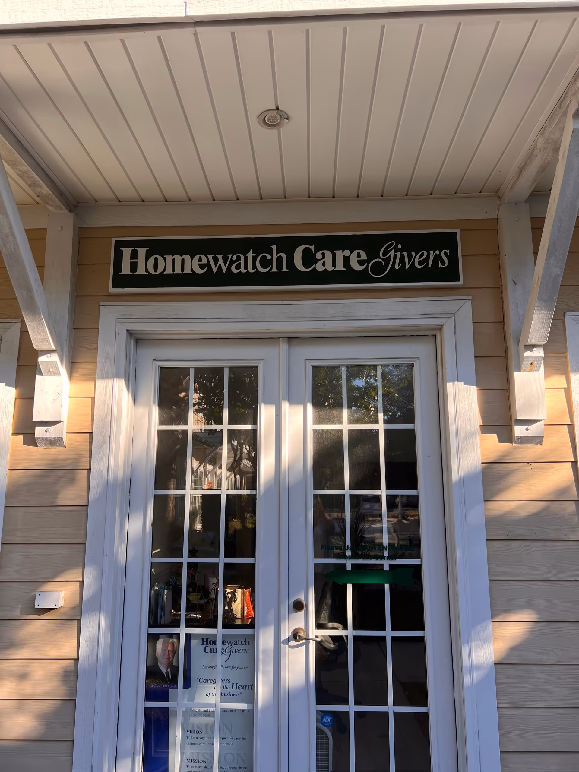 Front entrance of Homewatch CareGivers building with glass double doors and sign.