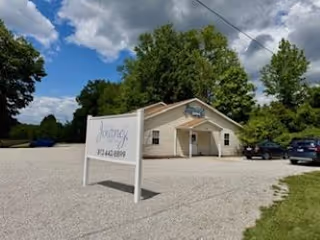 Small beige senior care building with gravel lot and a sign.