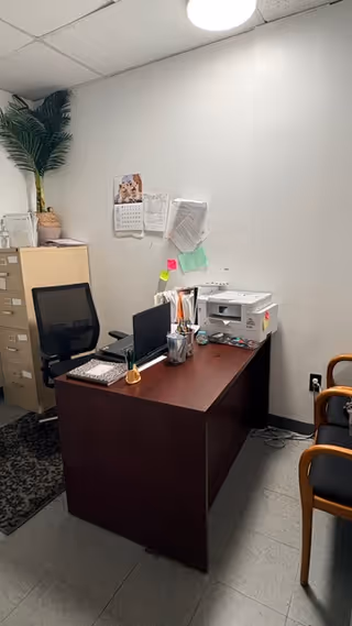 A small office in a senior living facility with desk, computer, printer, and plant.