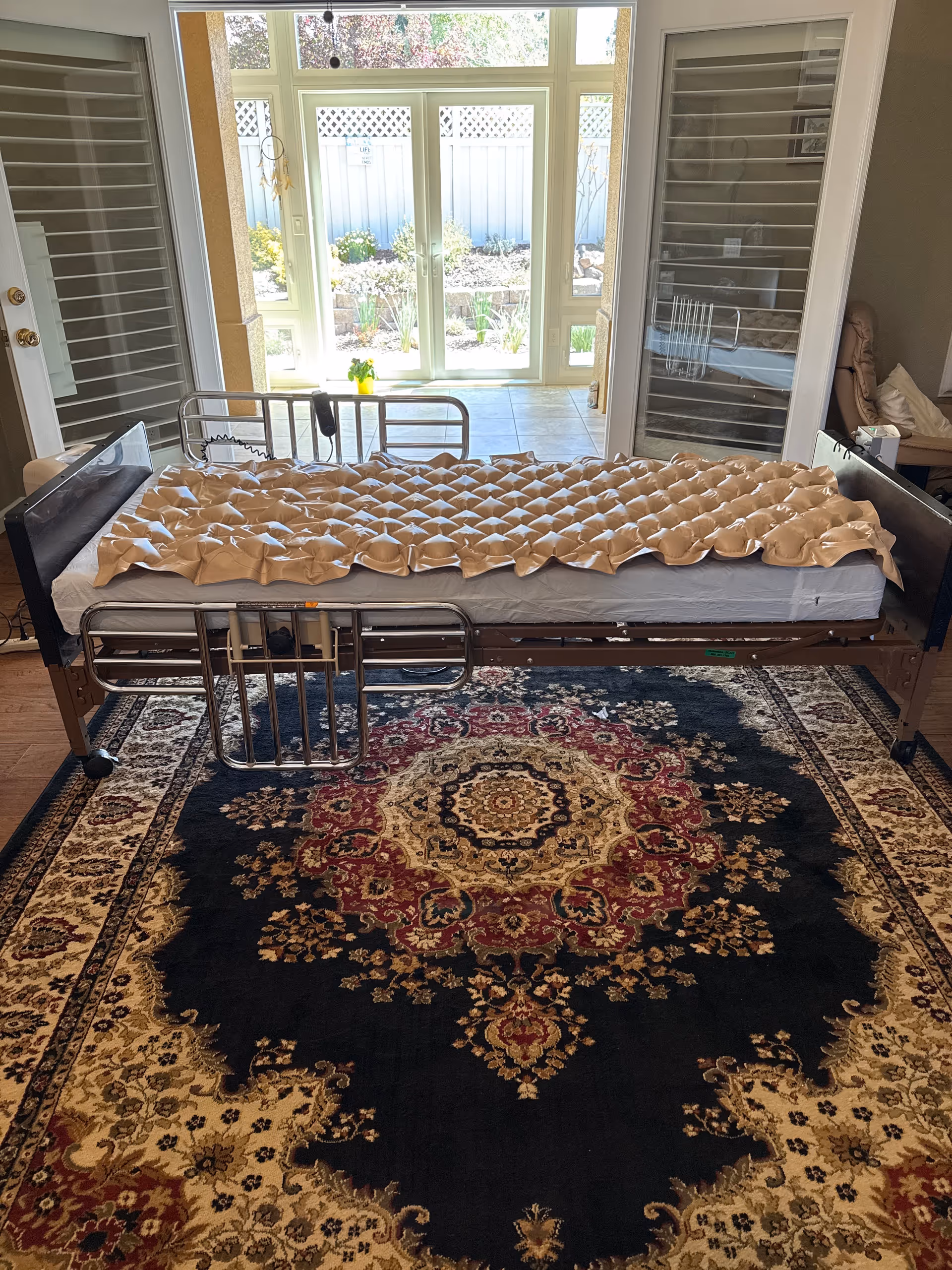 Hospital-style bed in a bright bedroom with large glass doors to an outdoor area.