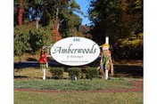Two people pose beside the Amberwoods of Farmington sign on a landscaped lawn.