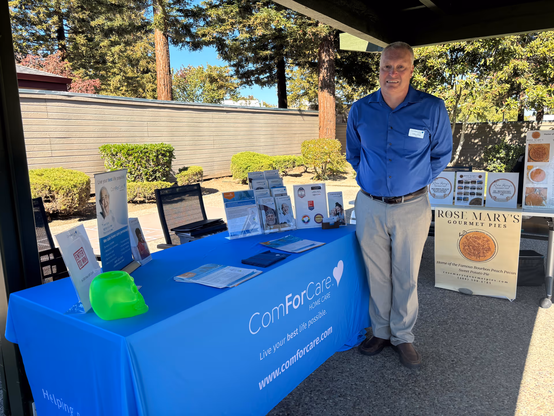 ComForCare promotional booth outdoors with a staff member beside a blue table and brochures.