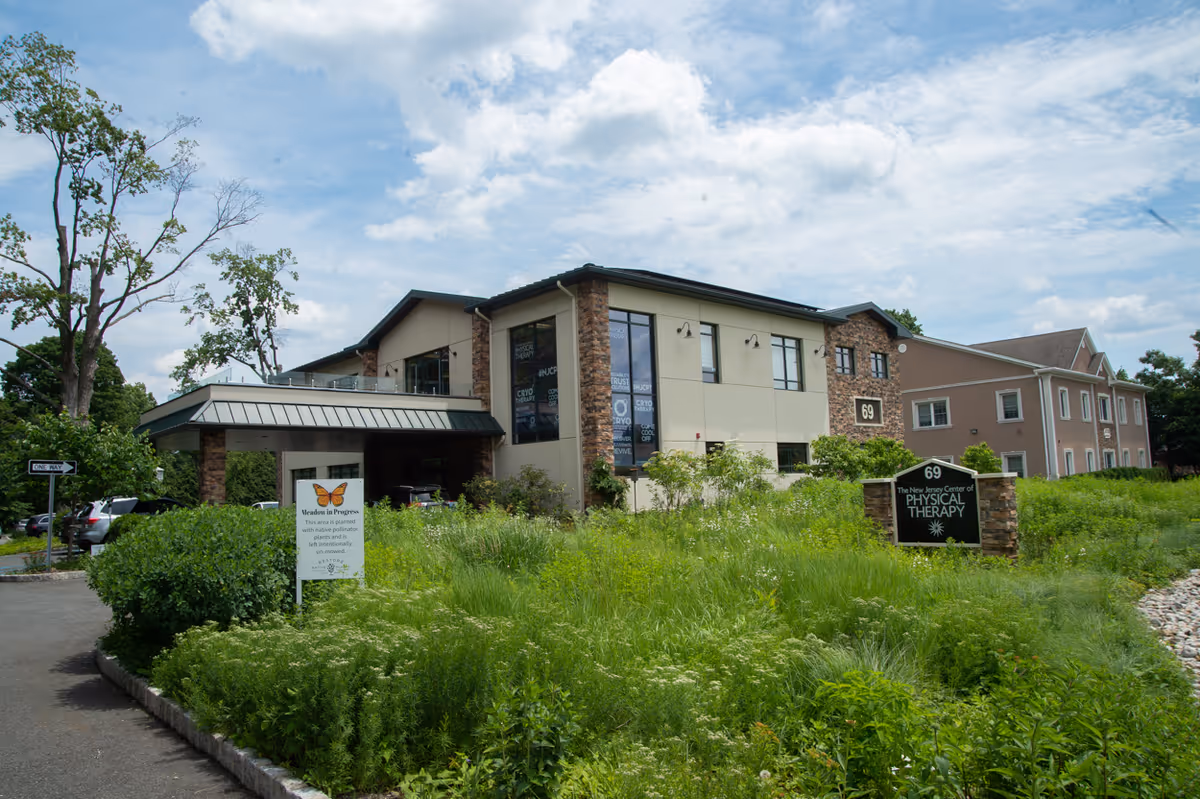 Modern two-story building with brick and beige siding, greenery, and a Physical Therapy sign.